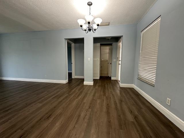 unfurnished dining area with dark wood-type flooring, a textured ceiling, and an inviting chandelier