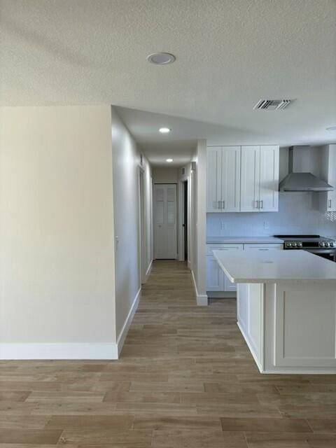 kitchen featuring wall chimney range hood, a kitchen island, light hardwood / wood-style flooring, stainless steel electric range, and white cabinets