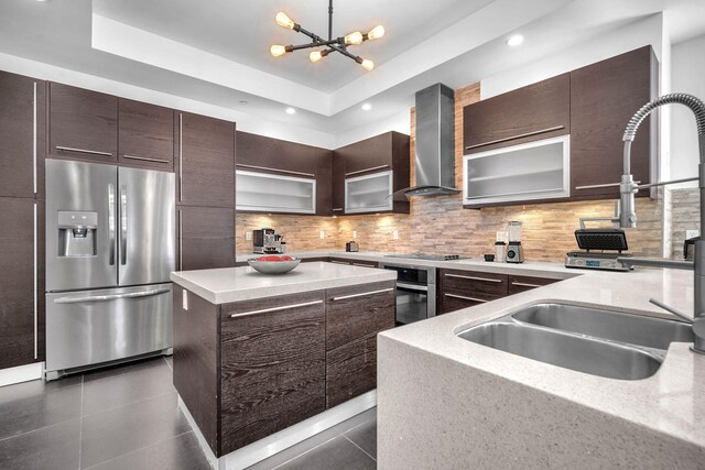 kitchen featuring decorative backsplash, appliances with stainless steel finishes, a tray ceiling, wall chimney range hood, and a center island