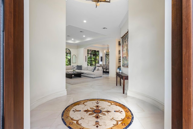 corridor featuring an inviting chandelier, a tray ceiling, and ornamental molding