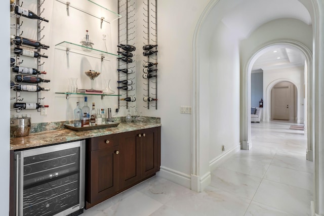 bar featuring ornamental molding, beverage cooler, light stone countertops, and dark brown cabinets