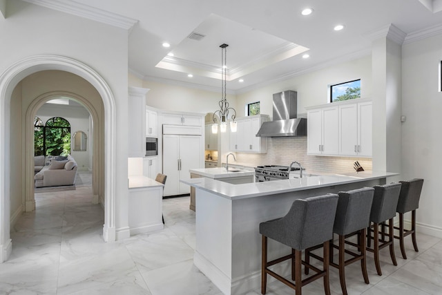 kitchen featuring pendant lighting, a breakfast bar area, white cabinetry, built in appliances, and wall chimney exhaust hood