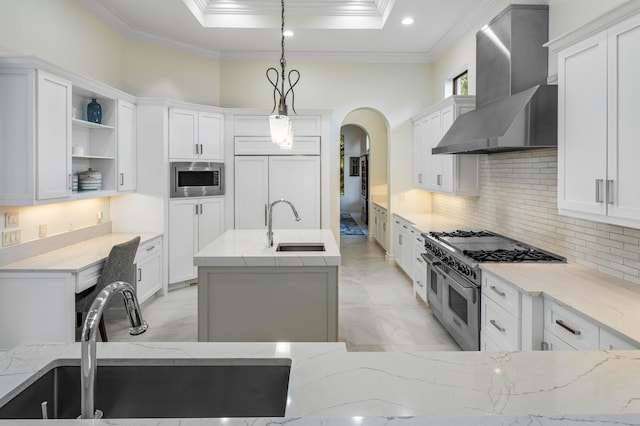 kitchen featuring hanging light fixtures, white cabinetry, built in appliances, and wall chimney exhaust hood