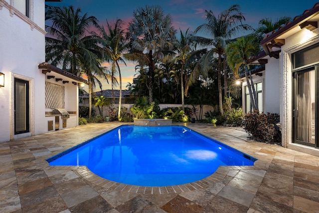 pool at dusk with an outdoor kitchen and a patio