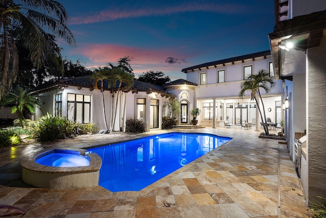 pool at dusk with an in ground hot tub and a patio area