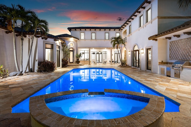 pool at dusk with an in ground hot tub, an outdoor kitchen, a grill, and a patio area