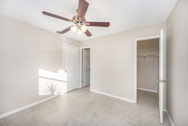 unfurnished bedroom with a walk in closet, a textured ceiling, and ceiling fan