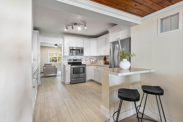 kitchen with white cabinetry, stainless steel appliances, crown molding, decorative backsplash, and a breakfast bar