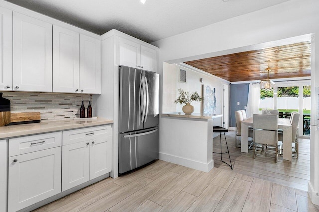 kitchen with light stone countertops, tasteful backsplash, wood ceiling, white cabinets, and stainless steel refrigerator