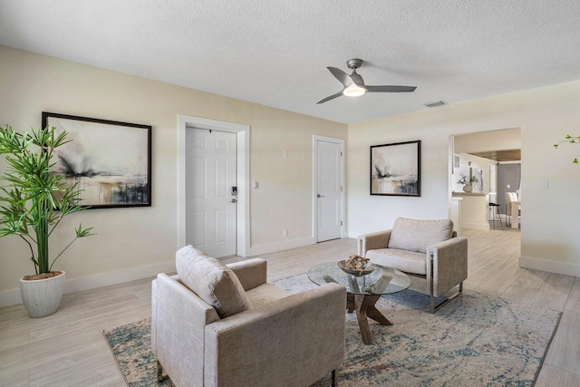 living room featuring ceiling fan, a textured ceiling, and light wood-type flooring