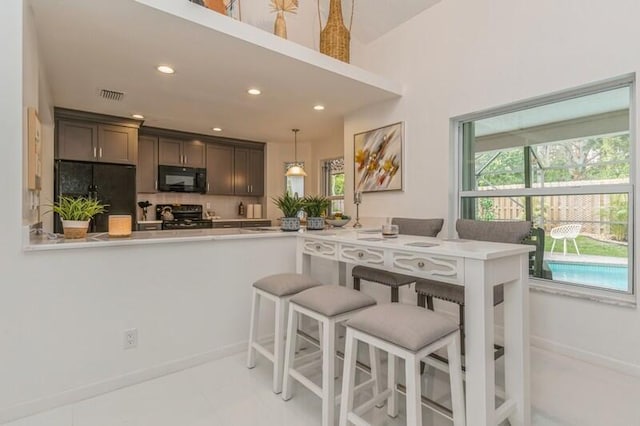 kitchen featuring backsplash, pendant lighting, black appliances, kitchen peninsula, and a breakfast bar area