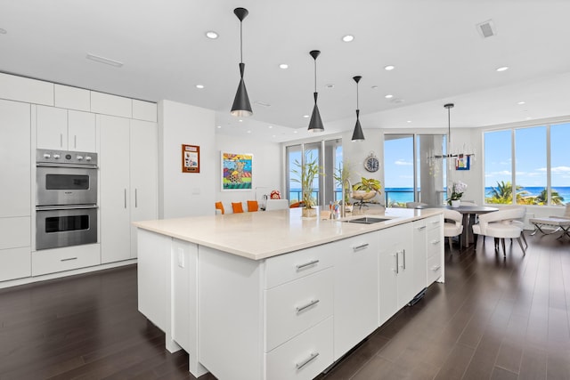 kitchen featuring double oven, white cabinetry, a center island with sink, and pendant lighting