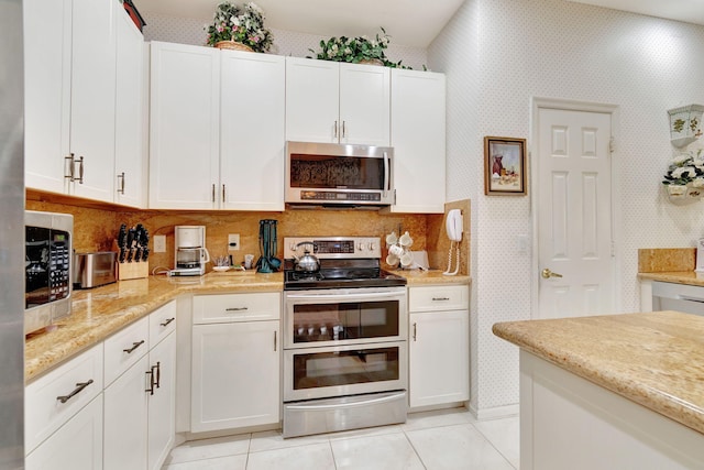 kitchen featuring light stone countertops, white cabinetry, light tile patterned floors, and stainless steel appliances