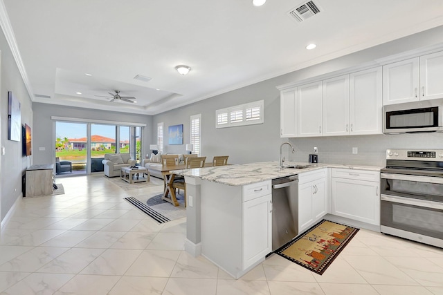 kitchen with appliances with stainless steel finishes, light stone countertops, kitchen peninsula, white cabinets, and a raised ceiling