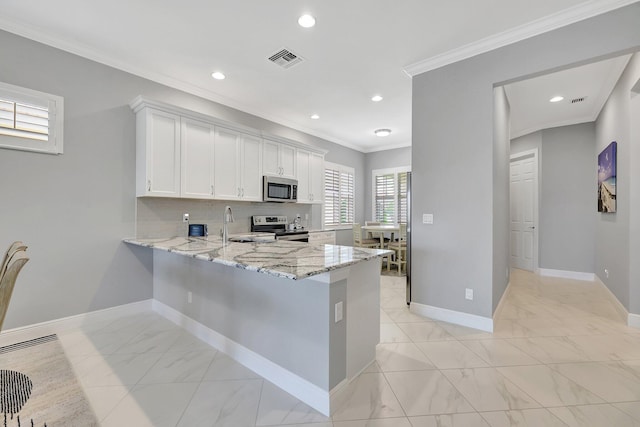 kitchen with white cabinets, ornamental molding, light stone counters, kitchen peninsula, and stainless steel appliances