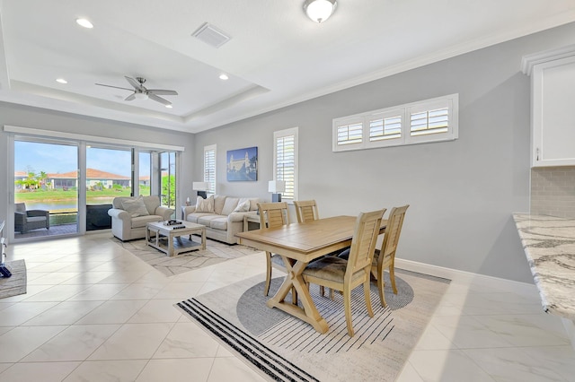 dining space with a water view, ornamental molding, a tray ceiling, and a wealth of natural light