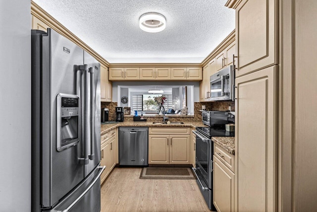 kitchen with stainless steel appliances, light wood-type flooring, light stone countertops, and sink