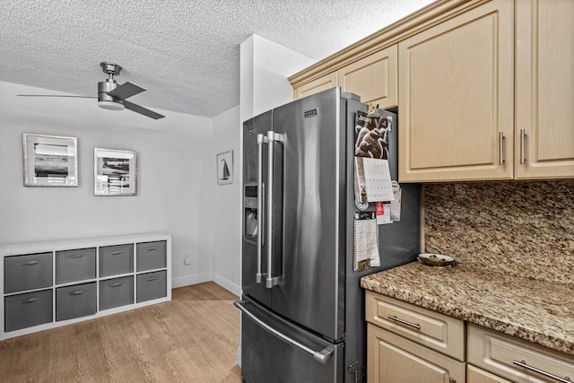 kitchen featuring ceiling fan, light stone counters, high quality fridge, light hardwood / wood-style flooring, and backsplash