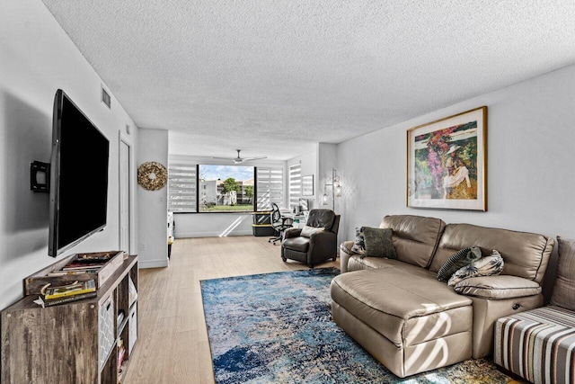 living room with a textured ceiling, ceiling fan, and light hardwood / wood-style flooring