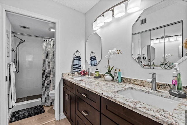 bathroom featuring toilet, wood-type flooring, vanity, a textured ceiling, and curtained shower