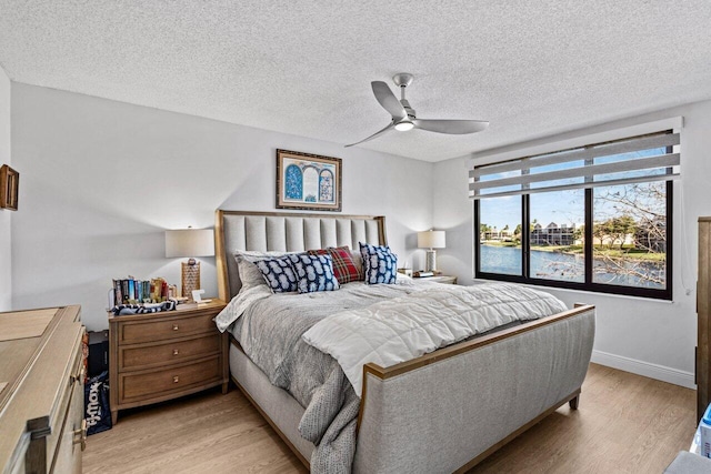 bedroom with ceiling fan, light hardwood / wood-style floors, a water view, and a textured ceiling