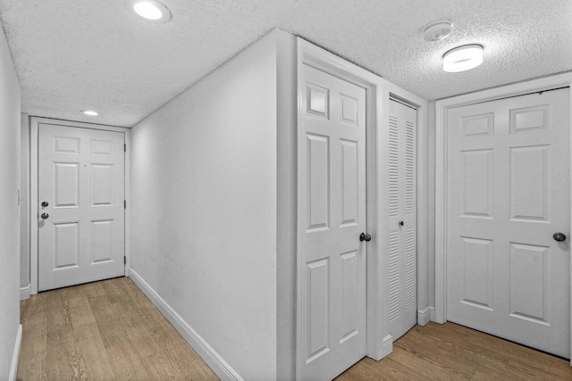 hallway with a textured ceiling and light hardwood / wood-style floors