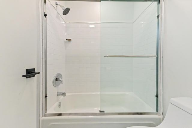 bathroom featuring combined bath / shower with glass door and toilet