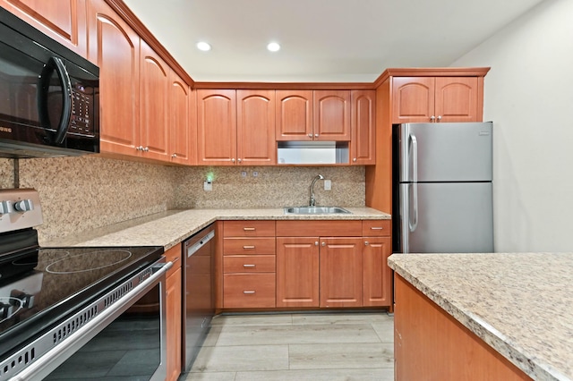 kitchen with appliances with stainless steel finishes, decorative backsplash, sink, light wood-type flooring, and light stone counters