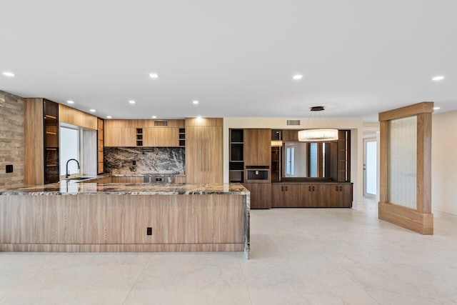 kitchen with hanging light fixtures, oven, tasteful backsplash, light stone countertops, and kitchen peninsula