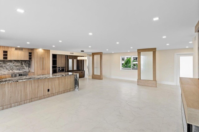 kitchen featuring light stone countertops, backsplash, and light brown cabinetry