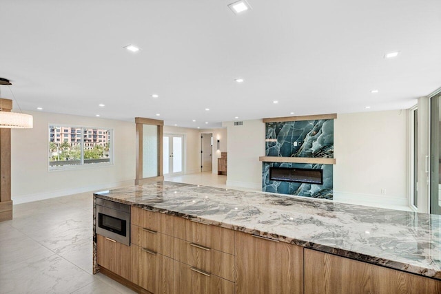 kitchen with stainless steel microwave, hanging light fixtures, light stone counters, and a premium fireplace