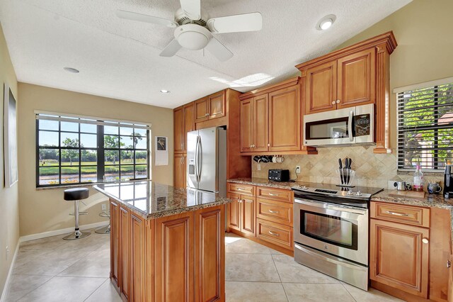 kitchen featuring a kitchen island, light stone counters, light tile patterned floors, and appliances with stainless steel finishes