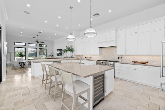 kitchen with ceiling fan, a center island with sink, white cabinetry, hanging light fixtures, and beverage cooler