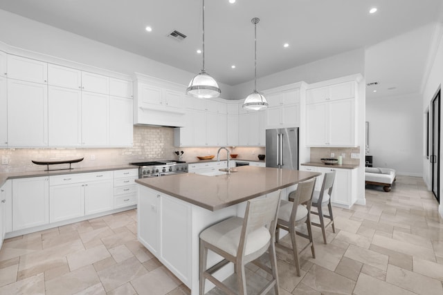 kitchen with decorative light fixtures, sink, a kitchen island with sink, premium appliances, and white cabinets