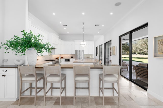 kitchen featuring a kitchen bar, an island with sink, stainless steel appliances, decorative light fixtures, and white cabinets