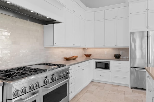 kitchen featuring high quality appliances, premium range hood, tasteful backsplash, and white cabinetry