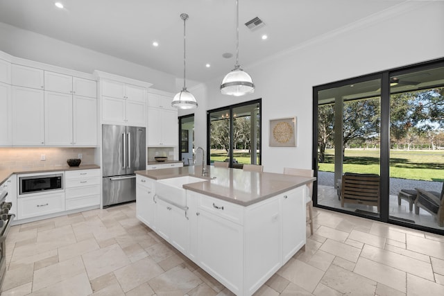 kitchen featuring a kitchen island with sink, built in microwave, stainless steel refrigerator, pendant lighting, and sink