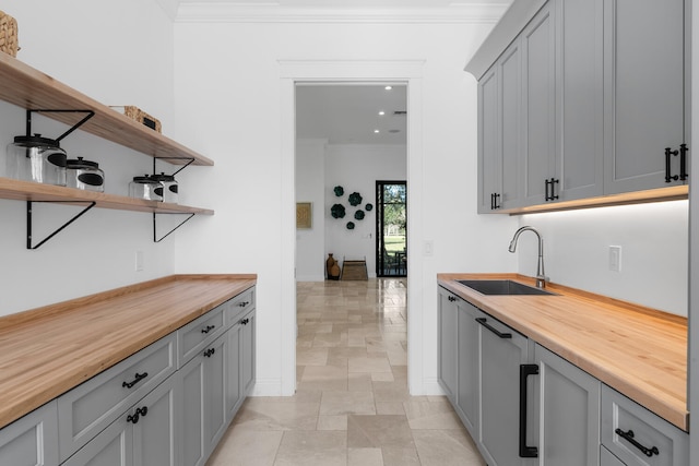 kitchen with gray cabinetry, ornamental molding, butcher block counters, and sink