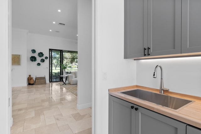 bar featuring ornamental molding, gray cabinetry, and sink