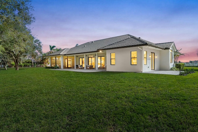 back house at dusk with ceiling fan, a patio area, and a yard