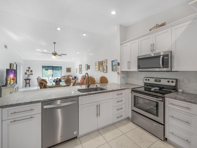 kitchen with kitchen peninsula, sink, lofted ceiling, and appliances with stainless steel finishes