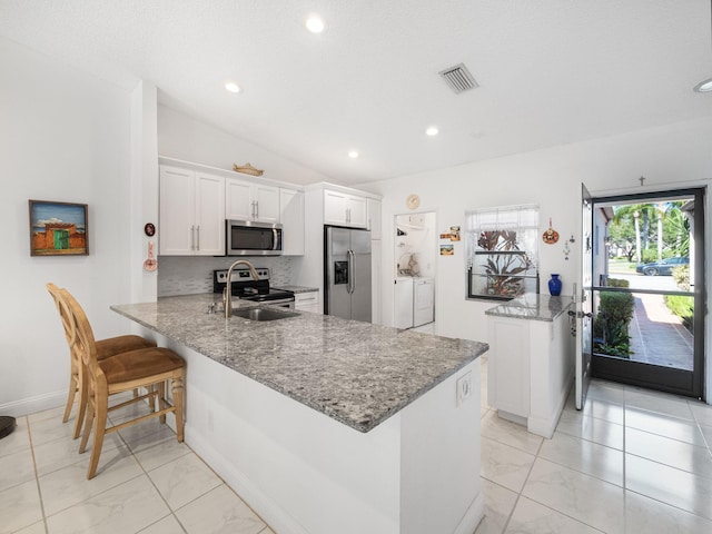 kitchen featuring stainless steel appliances, kitchen peninsula, vaulted ceiling, washer and clothes dryer, and white cabinets