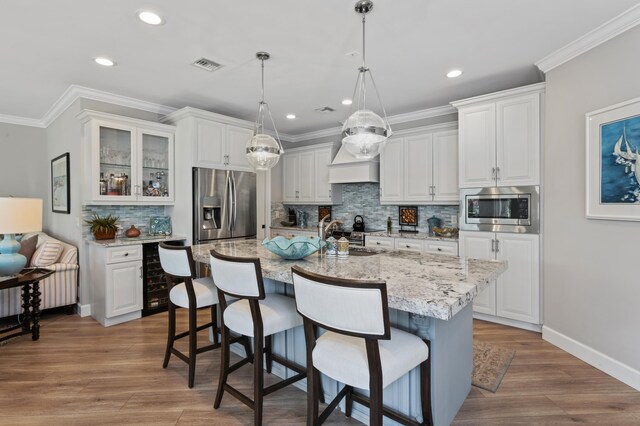 kitchen featuring a kitchen island with sink, white cabinetry, hanging light fixtures, and stainless steel appliances