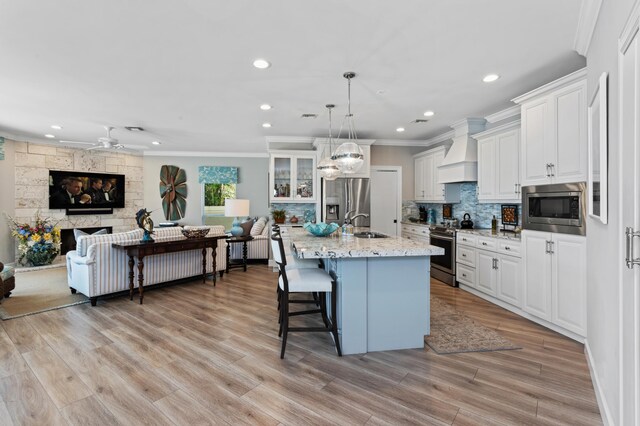 kitchen with a kitchen island with sink, white cabinets, stainless steel appliances, and custom exhaust hood