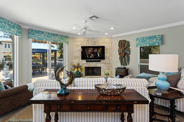 living room with a stone fireplace, ceiling fan, hardwood / wood-style flooring, and ornamental molding