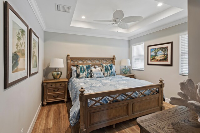 bedroom with a tray ceiling, ceiling fan, wood-type flooring, and ornamental molding