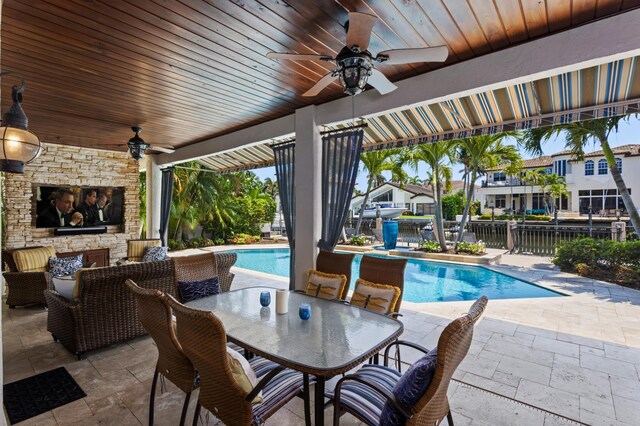 view of swimming pool featuring an outdoor stone fireplace, ceiling fan, and a patio