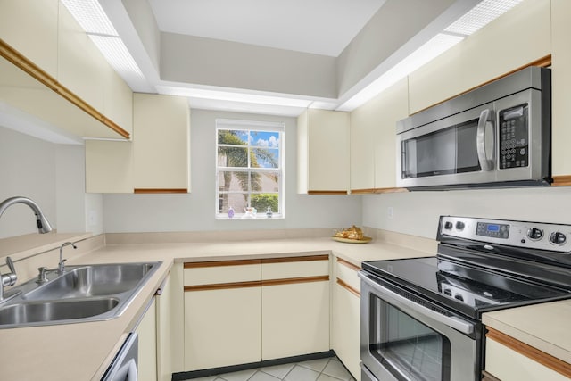 kitchen with sink, light tile patterned floors, stainless steel appliances, and cream cabinets