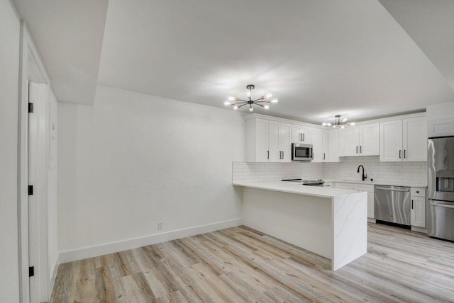 kitchen with kitchen peninsula, decorative backsplash, appliances with stainless steel finishes, a notable chandelier, and white cabinetry