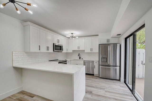 kitchen with kitchen peninsula, appliances with stainless steel finishes, sink, an inviting chandelier, and white cabinetry